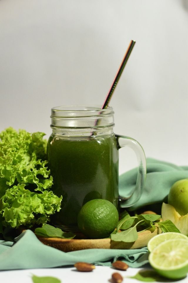Mason mug of lime lettuce green juice with limes and lettuce