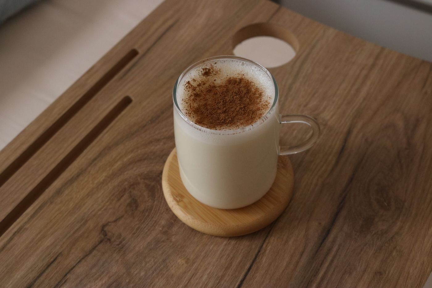 Glass mug of cinnamon-dusted cashew latte on a wooden tray