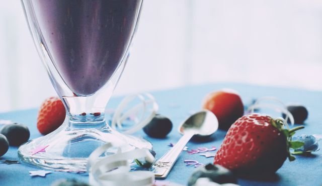 Purple berry shake in a footed glass with strawberries on blue