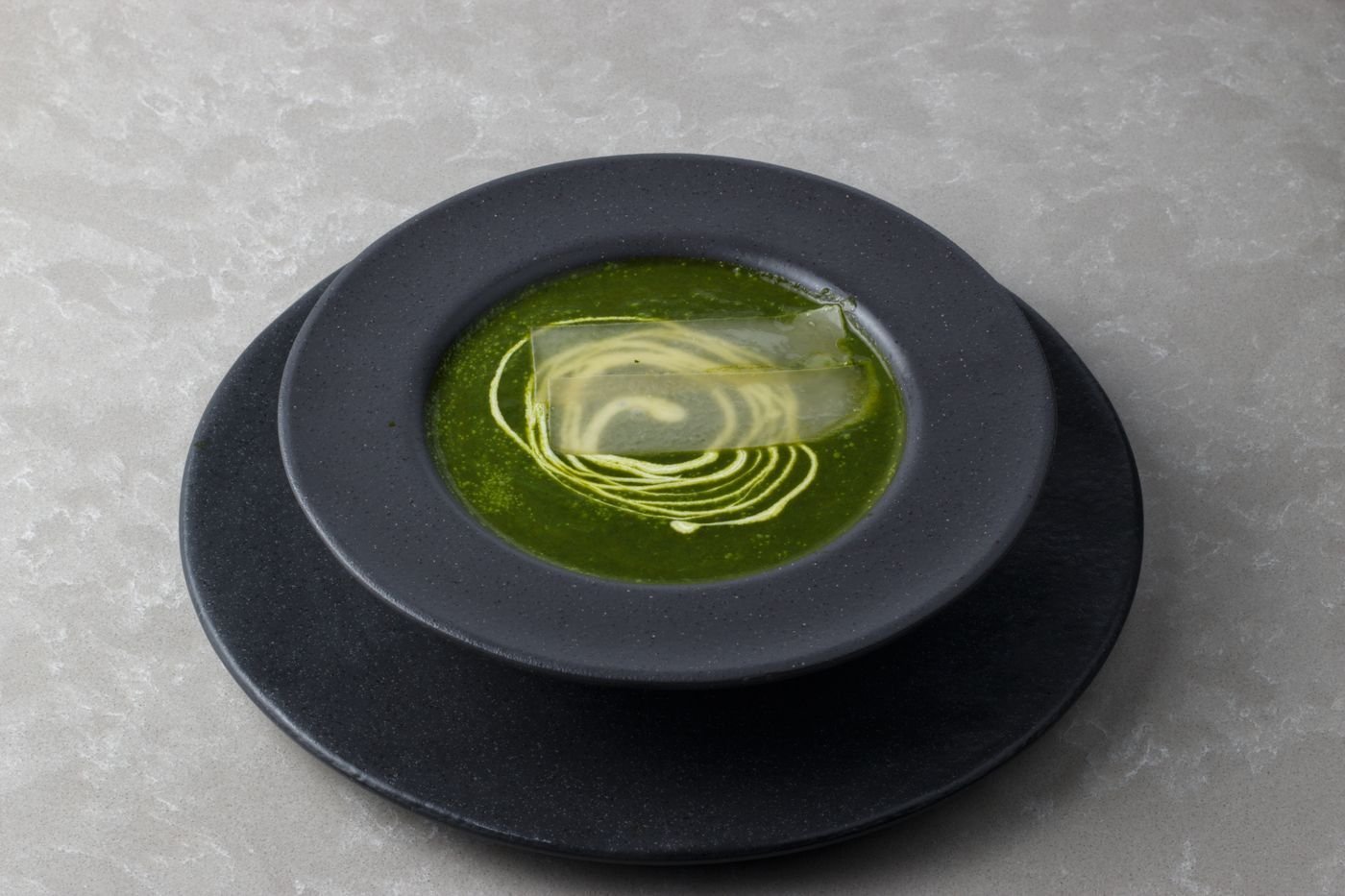 Dark green spinach coconut soup with a cream spiral in a black bowl