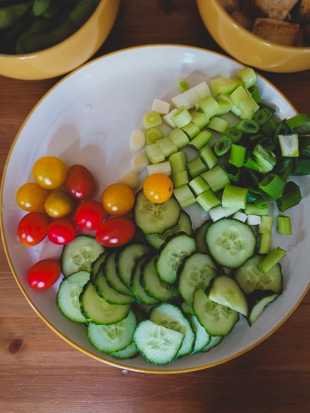 Bowl of sliced cucumbers, cherry tomatoes, celery and scallions
