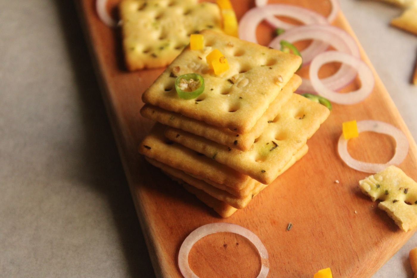 Stacked crackers with onion rings on a wooden board
