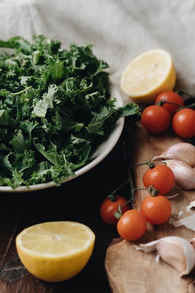 Bowl of chopped kale with lemons, cherry tomatoes and garlic on wood