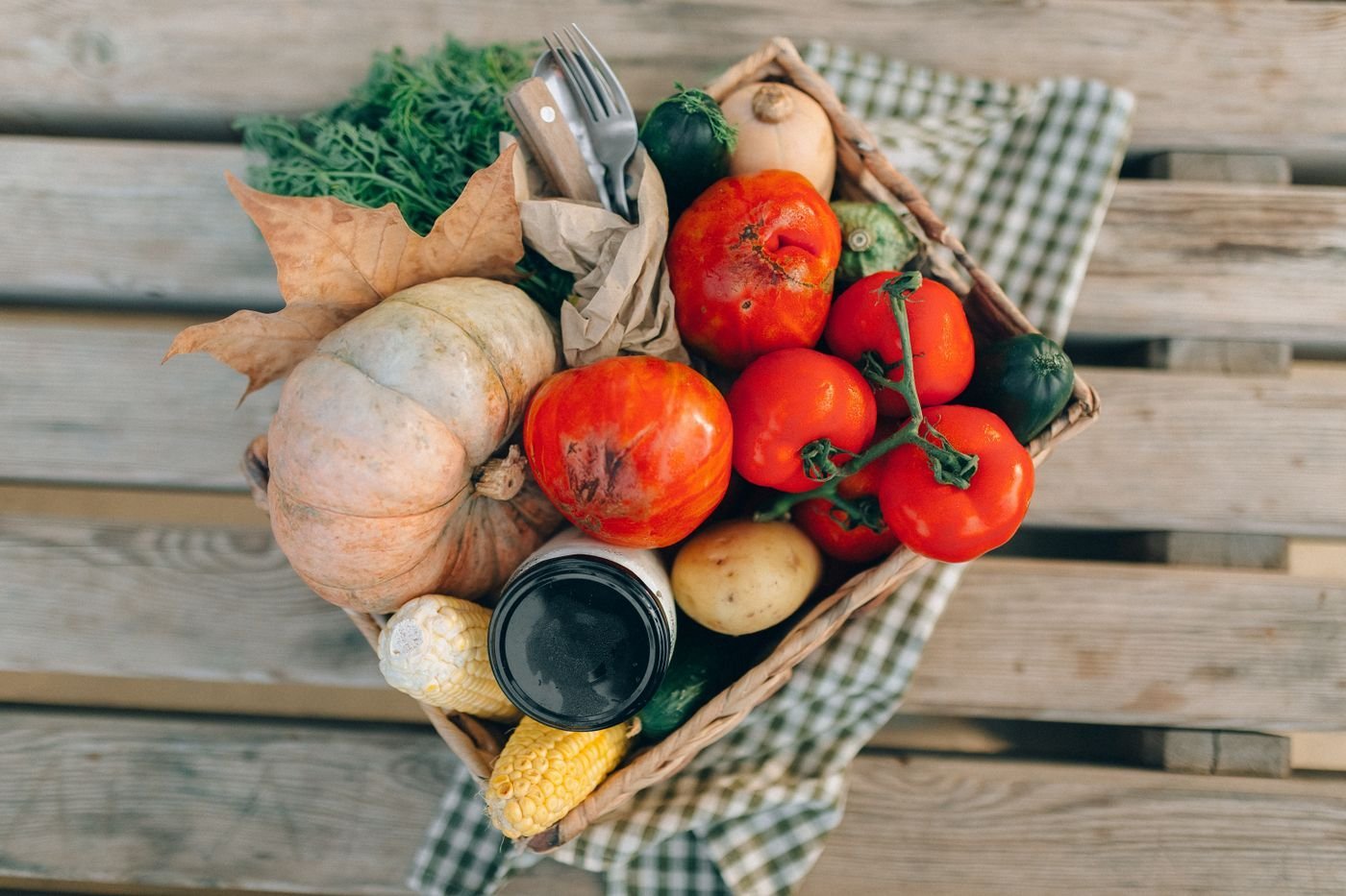 Wicker basket of tomatoes, pumpkin and root vegetables on weathered planks