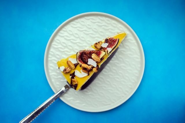 Fig, pistachio and mango tart slice on a white plate over bright blue