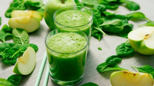 Two glasses of green apple spinach juice with apple slices